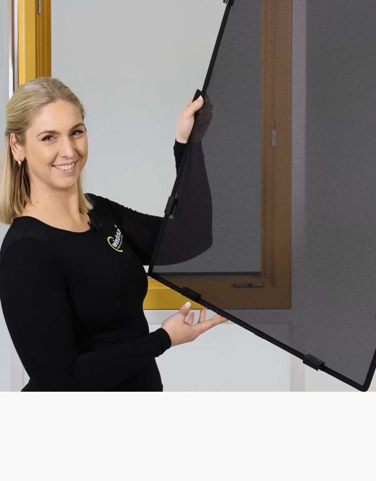 eine Frau hält lächelnd den WinClip vor einem Holzfenster in den Händen