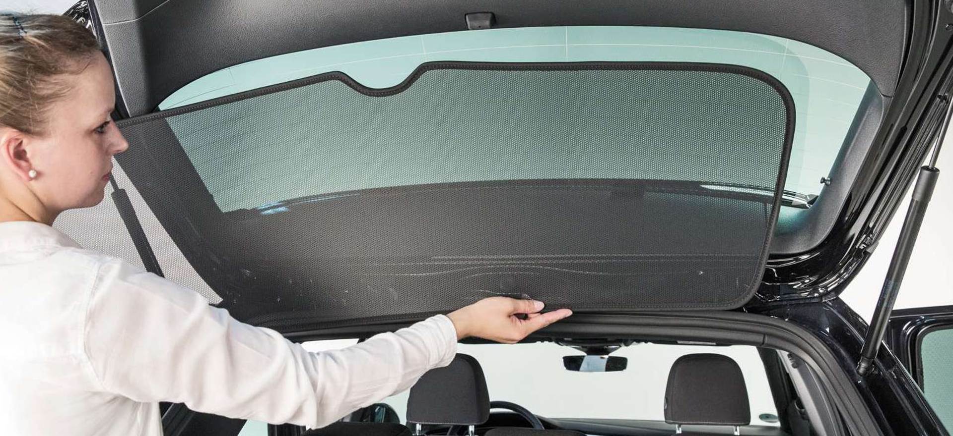 a woman places a sun protection element on the rear window of a car